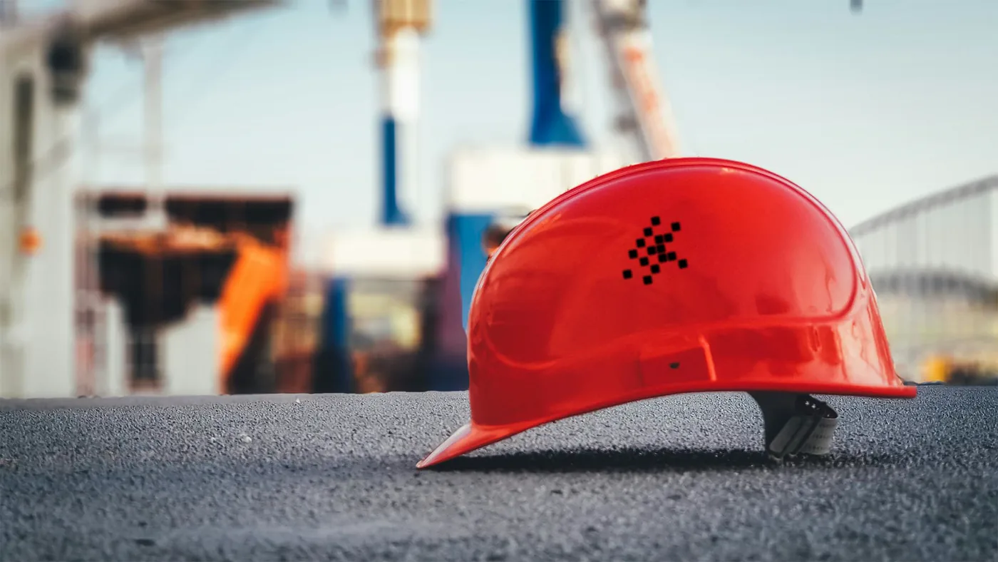 A red GSI Labs hard hat resting on the ground at a construction site