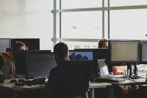 Developers at work in a shared office, code across several screens