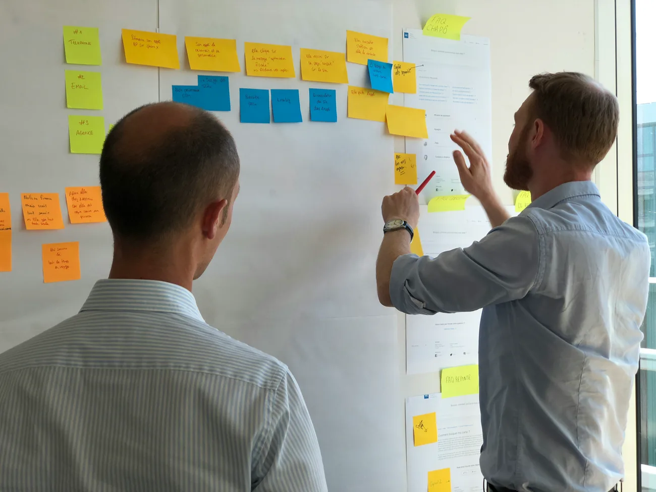 Two colleagues mapping a workflow across a wall of sticky notes