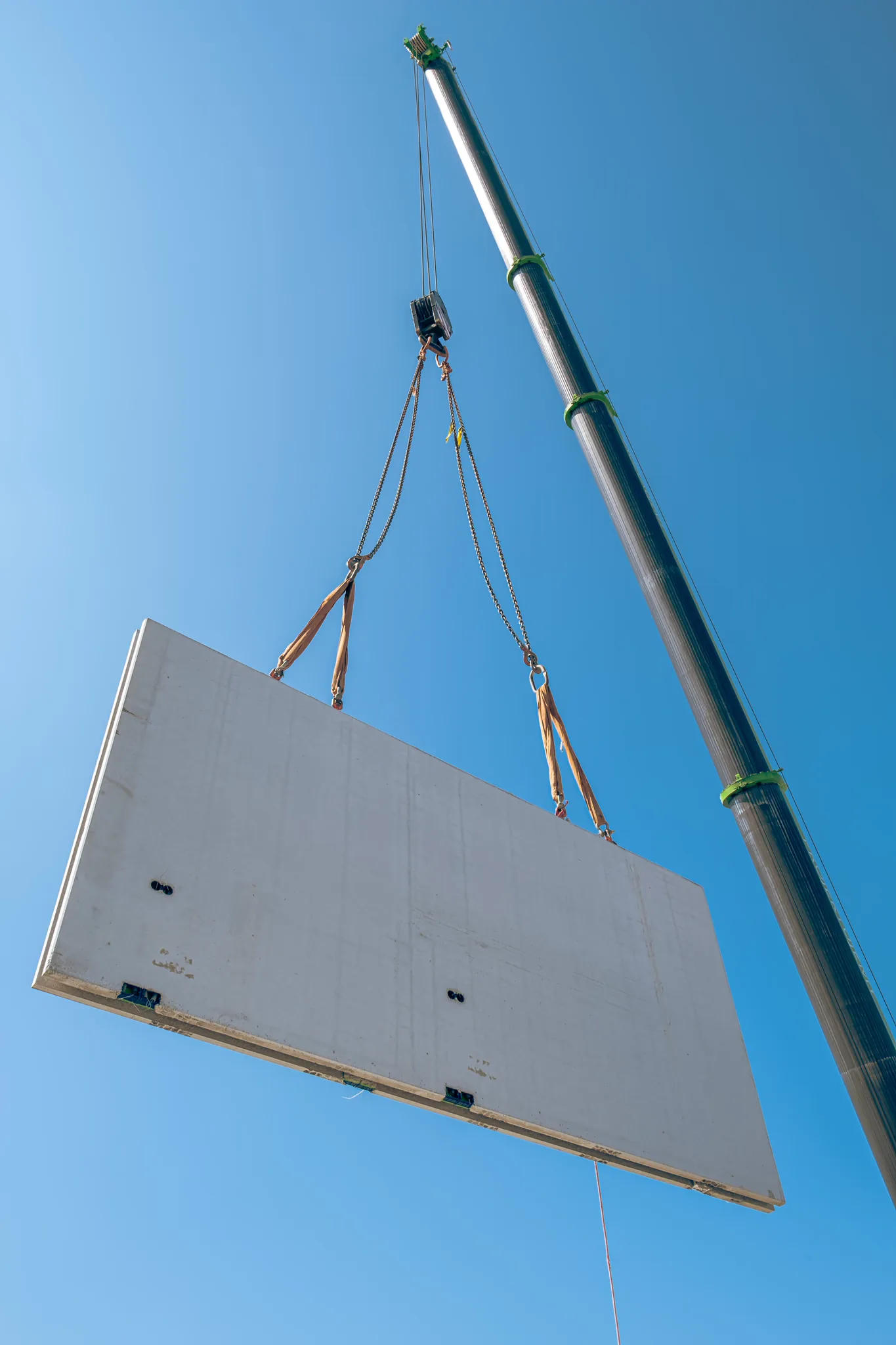 A precast wall panel on the crane hook against a clear sky